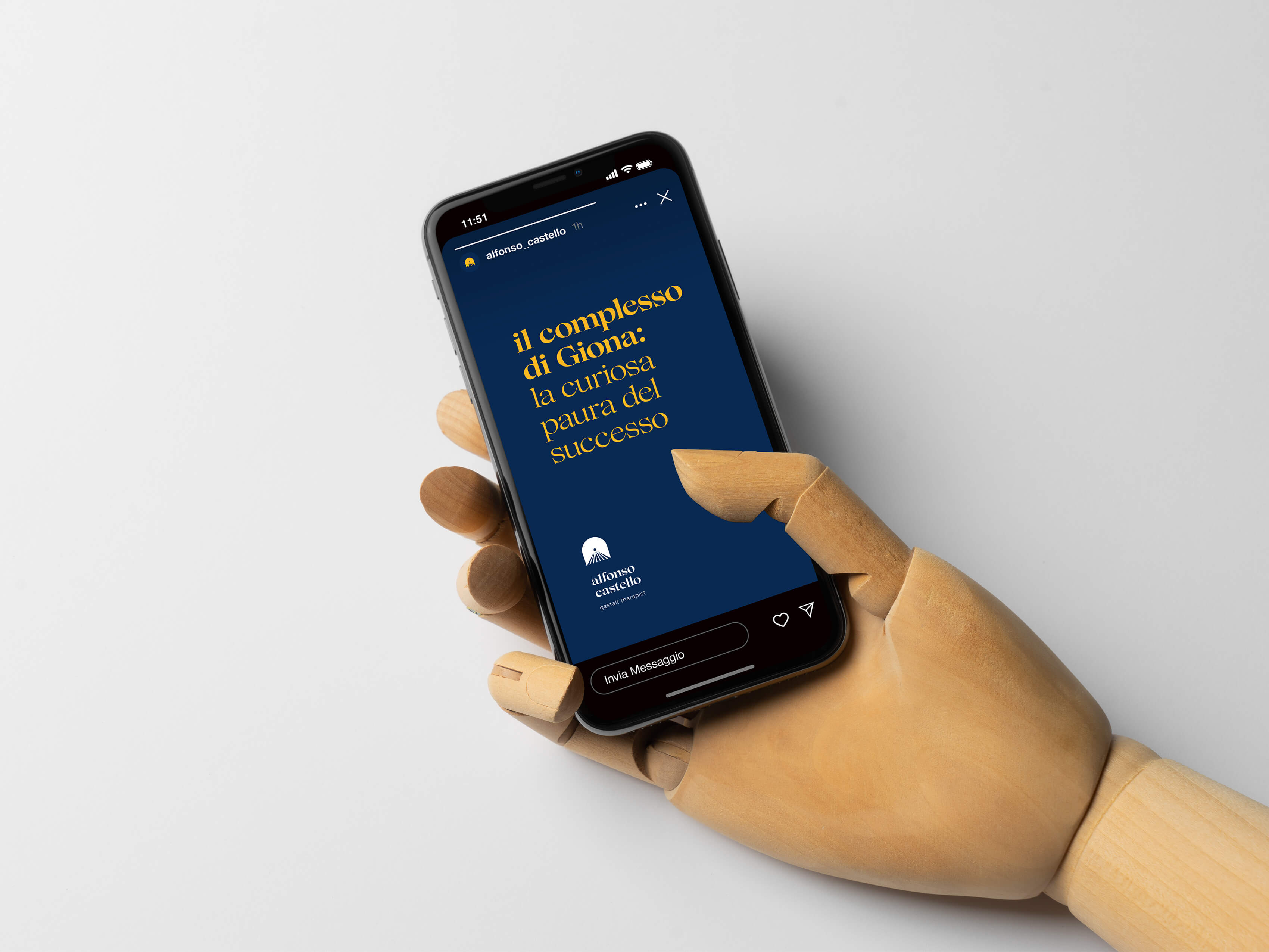 Mano di un manichino in legno che regge uno smartphone. Sullo schermo è visualizzato un esempio di story dello psicologo Alfonso Castello