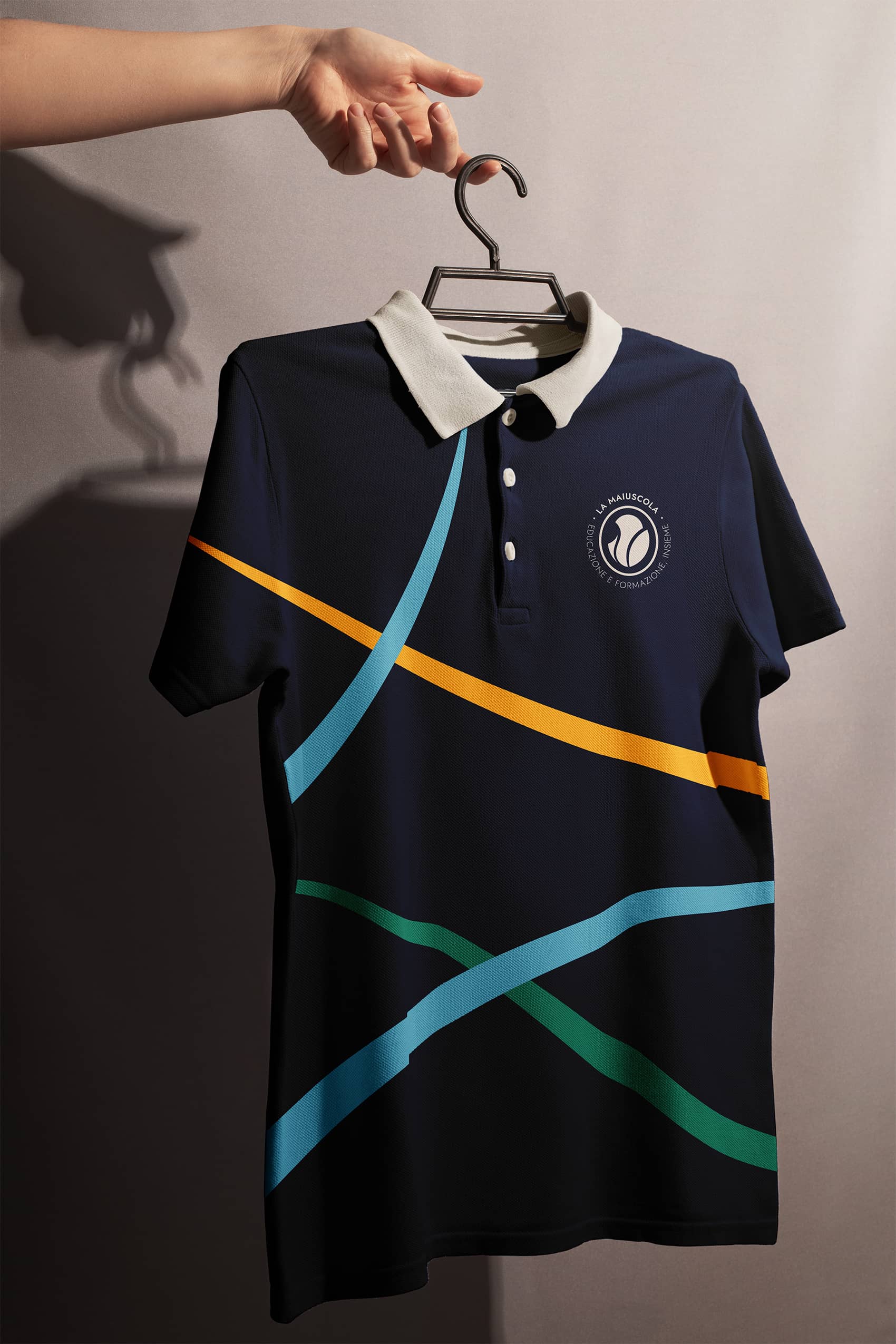 Navy blue polo shirt with white collar and colorful diagonal stripes in orange, light blue, and green, held on a hanger by a hand.