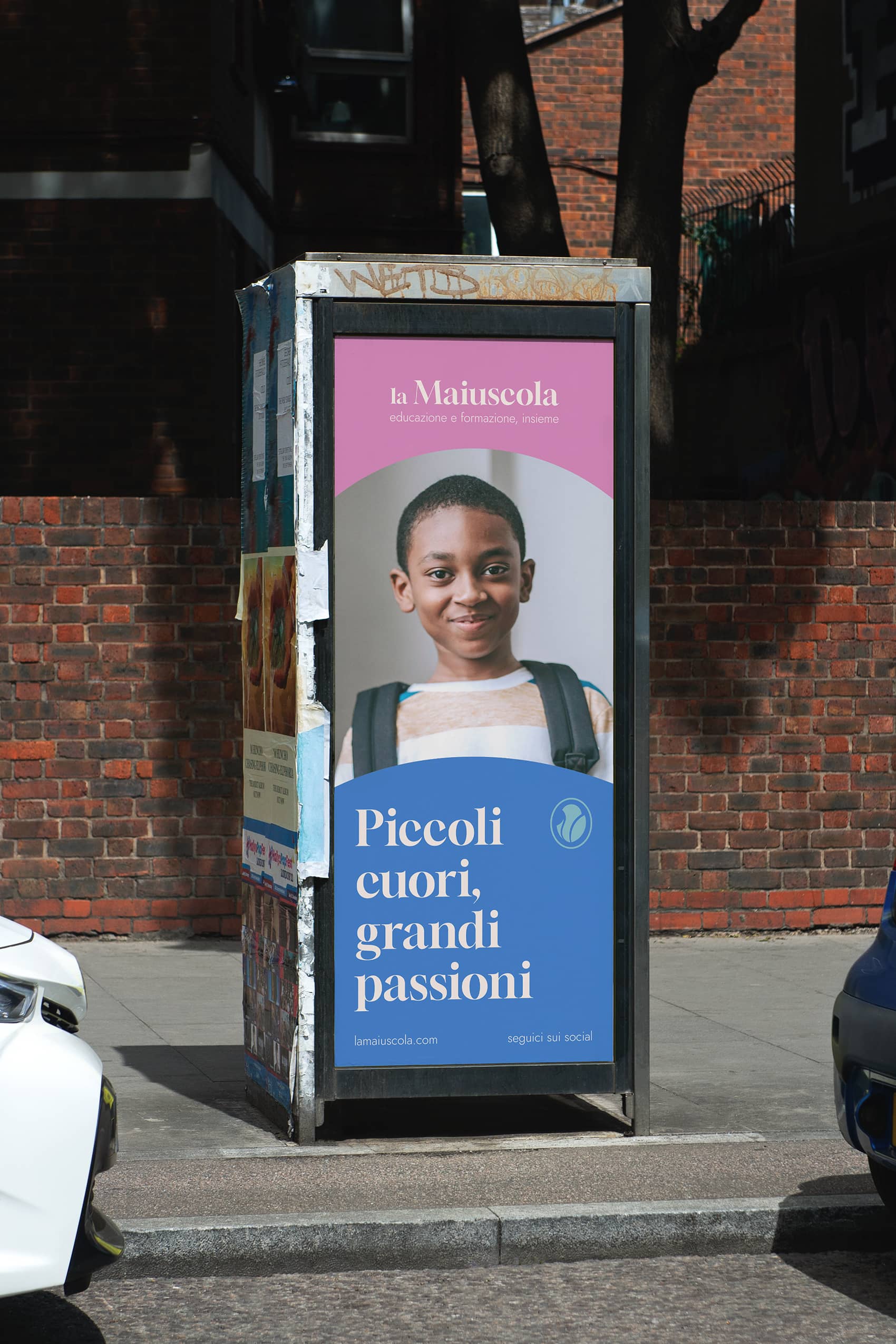 Street advertisement panel featuring a smiling boy with a backpack and Italian text promoting la Maiuscola education and training.