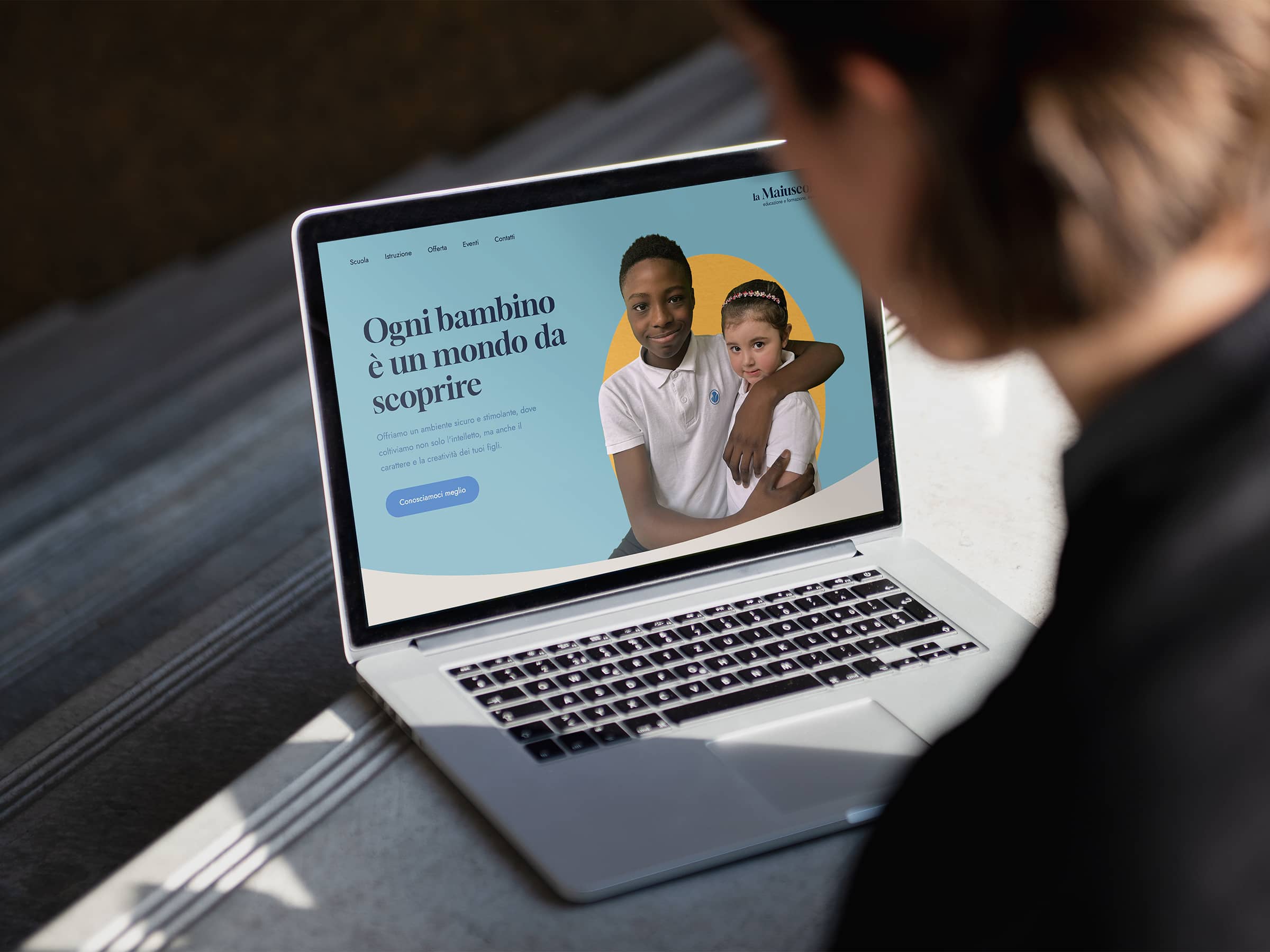 A person viewing a laptop displaying a webpage with two children and Italian text about child education.