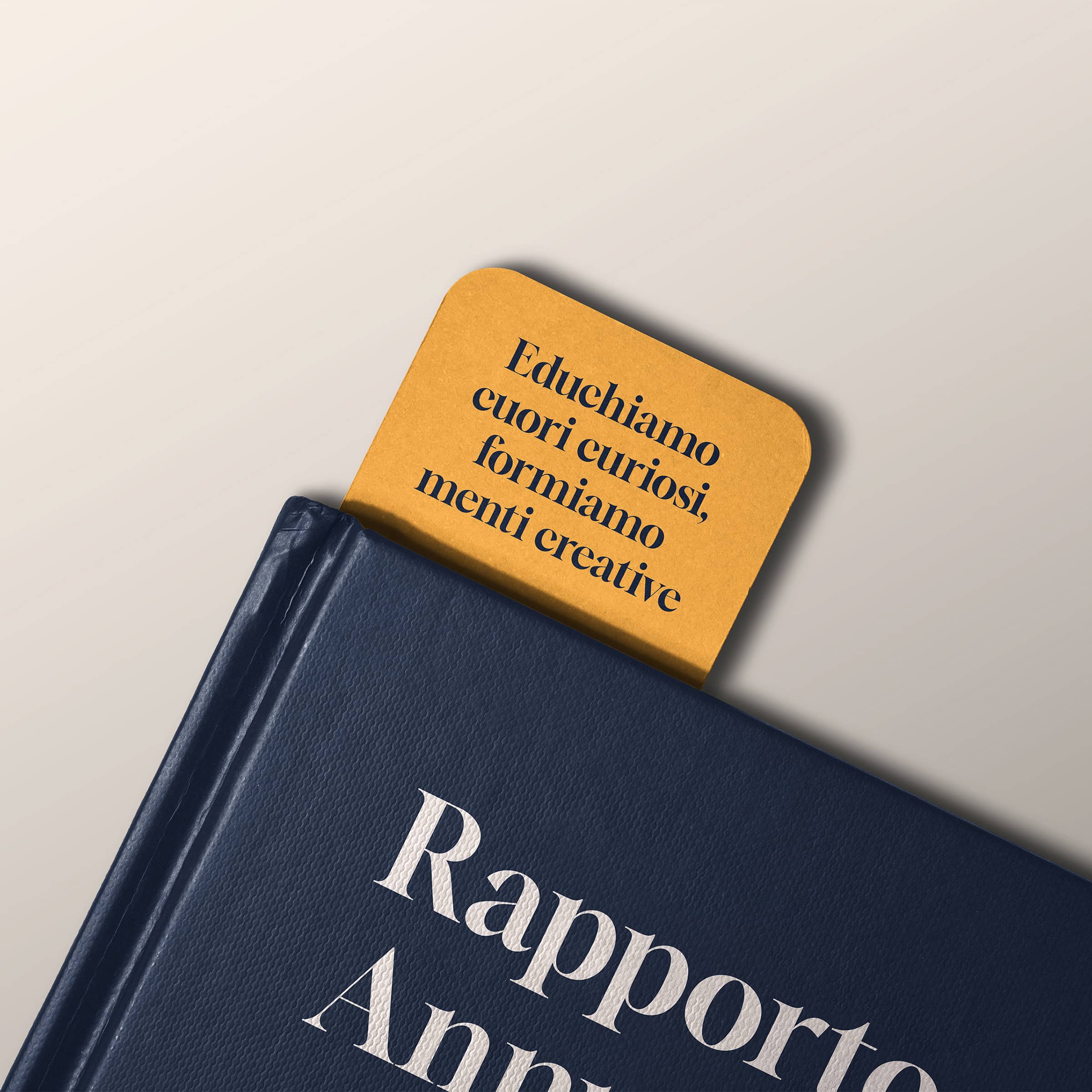 Corner of a dark blue book with a mustard yellow bookmark reading 'Educhiamo cuori curiosi, formiamo menti creative' in Italian.