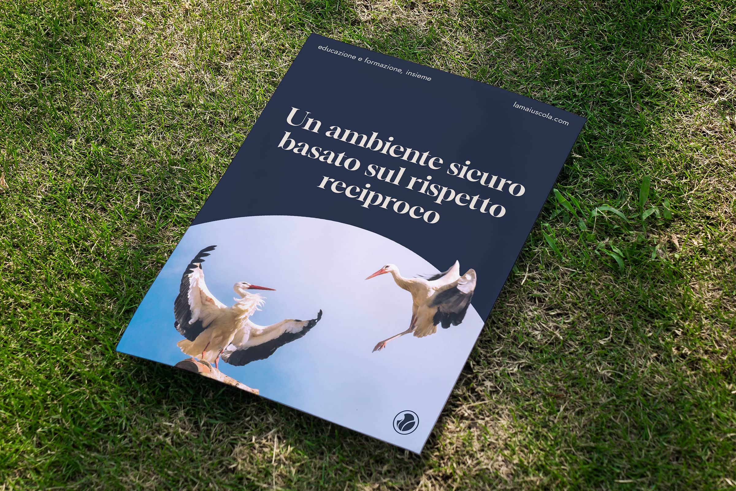 Brochure on grass showing two white storks with wings spread and Italian text about a safe environment based on mutual respect.