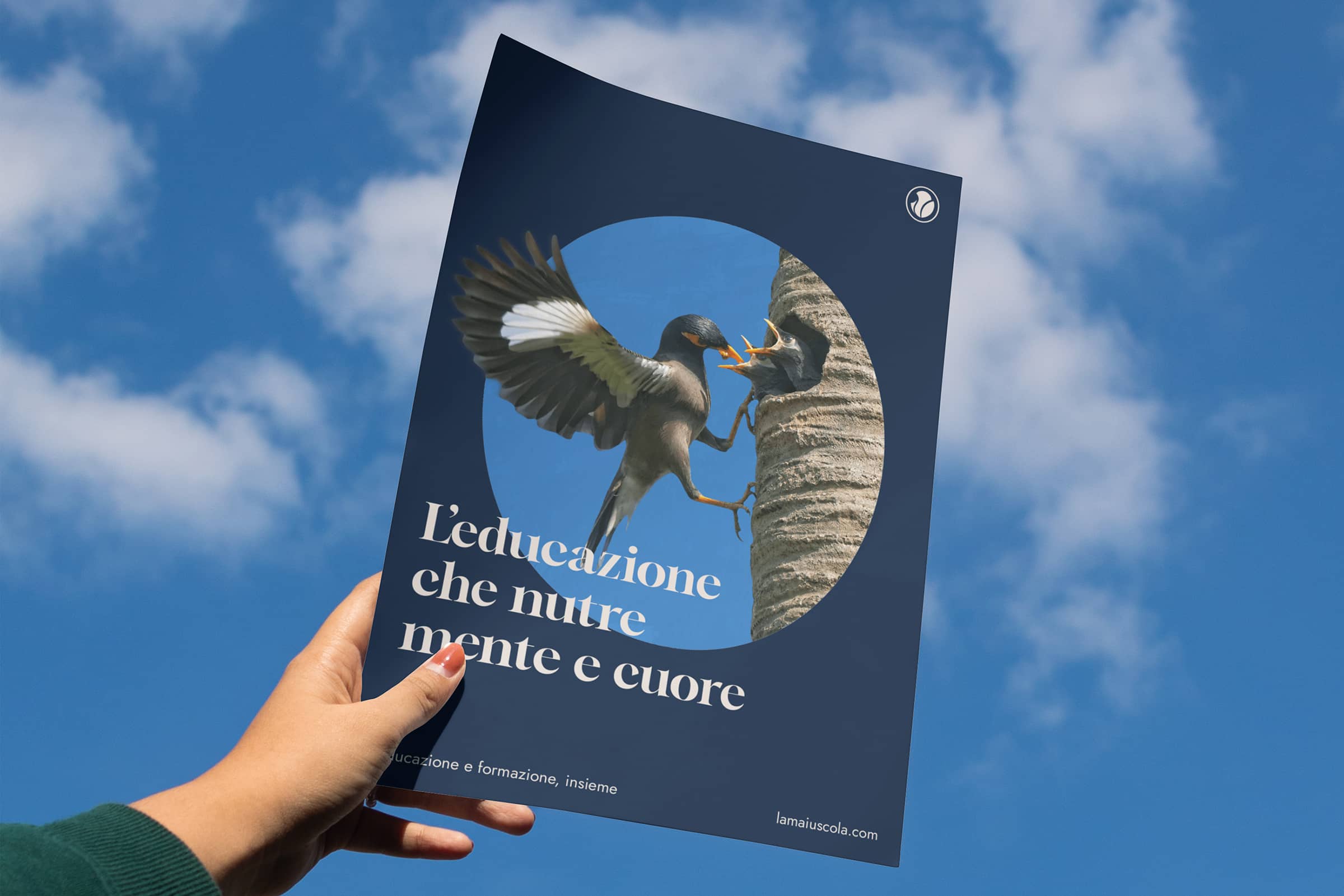 Hand holding a flyer against blue sky showing a bird feeding its chicks in a nest hole on a tree trunk with Italian text about education.