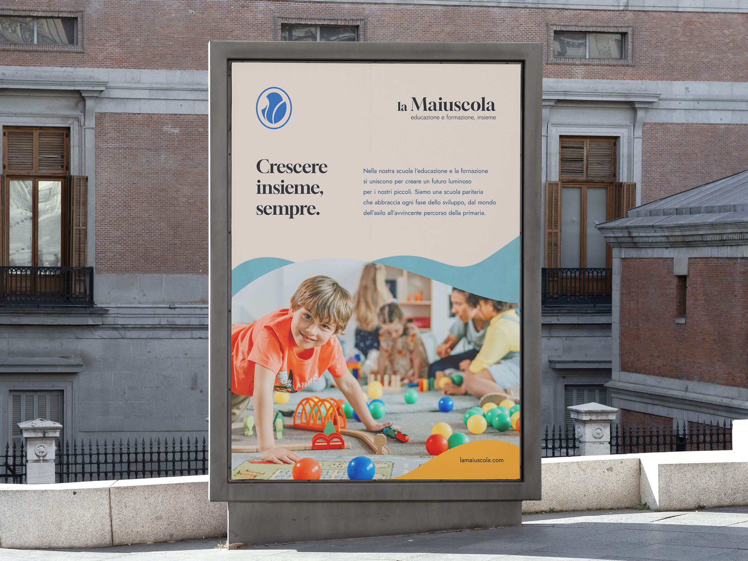 Outdoor billboard featuring a smiling boy in an orange shirt playing with colorful balls and toys indoors, with Italian text promoting education at la Maiuscola school.